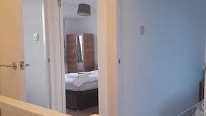 A bedroom with a bed, a wardrobe, and a hanging light fixture. - 3 bedroom London House (Dagenham)