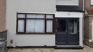 A two-story residential building with a white facade, large windows with brown frames, and a black front door. - 3 bedroom London House (Dagenham)