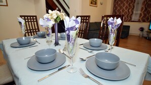 A dining table set with grey plates, bowls, and cutlery, accompanied by floral centerpieces in clear glass vases. - 3 bedroom London House (Dagenham)