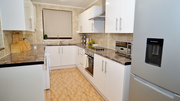 A modern kitchen with white cabinets, a granite countertop, and a built-in oven. - 3 bedroom London House (Dagenham)