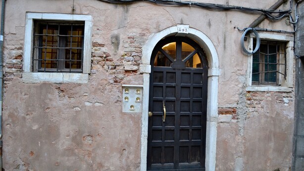 A building with a black door, a small window with a metal grid, and a number '695' above the door. - Charming home behind Piazza San Marco, panoramic view over the rooftops of Venice (Venezia)