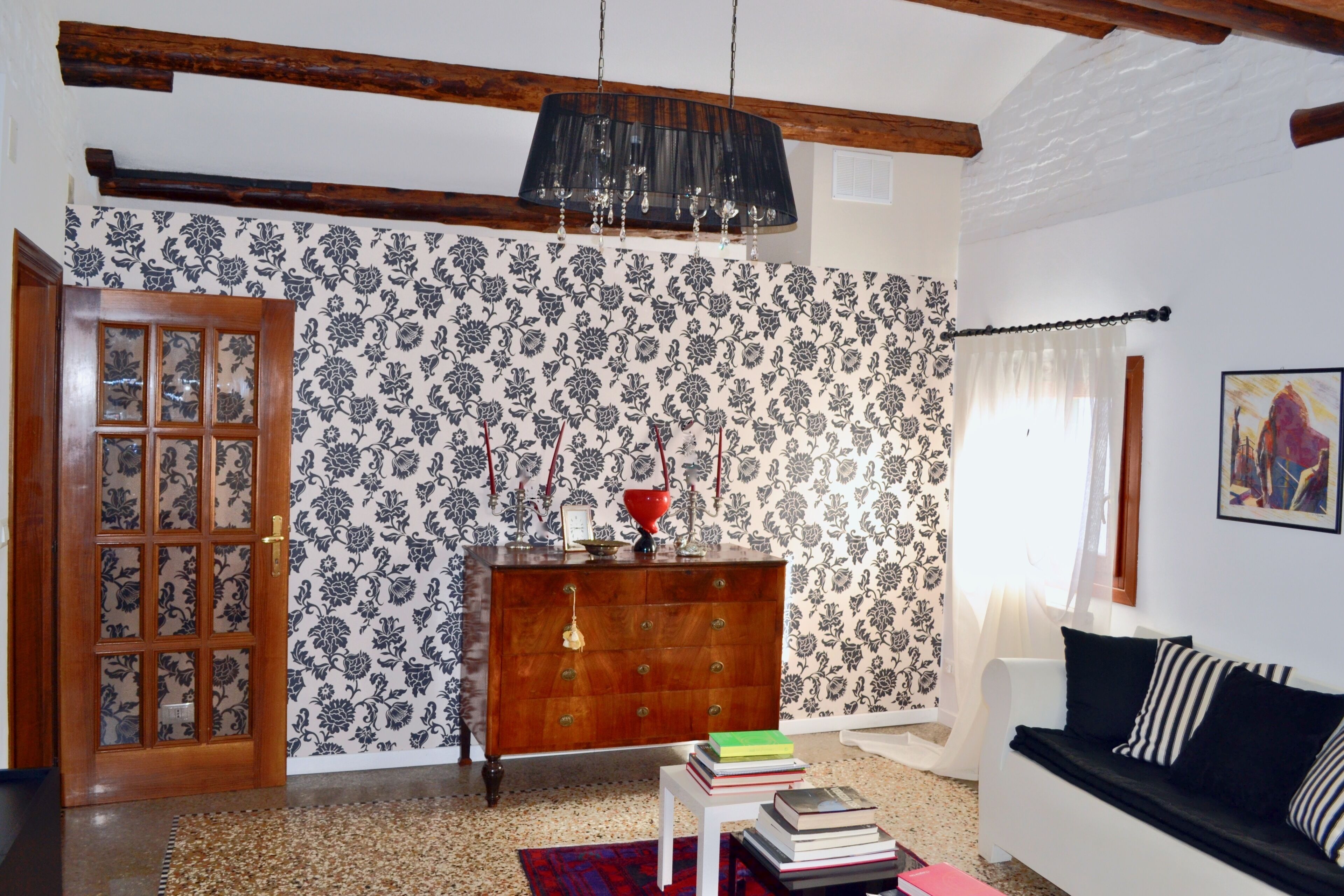 A living room with a wooden door, a patterned wallpaper, a wooden dresser, a white sofa, and a chandelier.