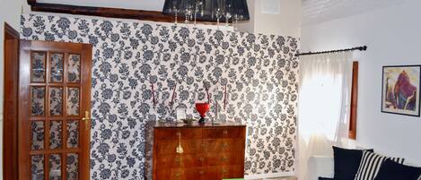 A living room with a wooden door, a patterned wallpaper, a wooden dresser, a white sofa, and a chandelier.