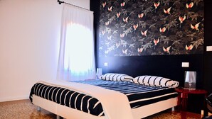 A bedroom with a bed, a nightstand, a lamp, and a wall with a floral pattern. - Charming home behind Piazza San Marco, panoramic view over the rooftops of Venice (Venezia)