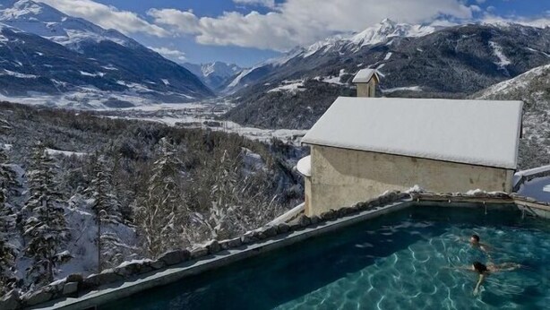 A pool with clear water surrounded by snow-covered mountains and a building with a snow-covered roof.