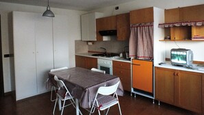 A compact kitchen with a dining table and chairs, a stove, and a television.