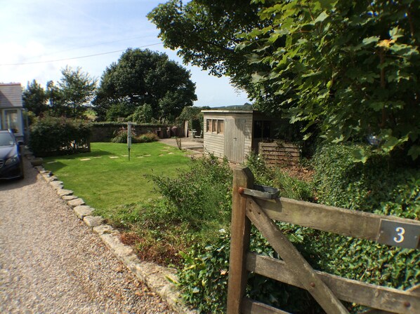 A rural property with a wooden gate marked '3', a small shed, and a car parked on a gravel path.