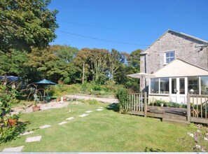 Stroll through the serene garden, surrounded by lush plants and a clear pathway, to the traditional stone house with a spacious conservatory.