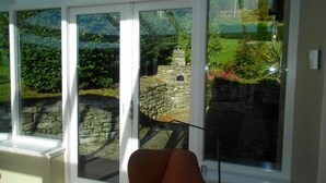 A room with large windows offering a view of a stone wall and greenery. - Former Lodge House to Swordale Castle (Evanton)