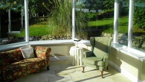 A conservatory with a view of a garden, a sofa, and a chair. - Former Lodge House to Swordale Castle (Evanton)