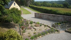 A rural landscape with a stone wall, gravel path, and a house with a sloped roof. - Former Lodge House to Swordale Castle (Evanton)