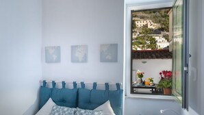Ein Schlafzimmer mit einem Bett, einem Fenster mit Blick auf Gebäude und einem kleinen Tisch mit Lampe.