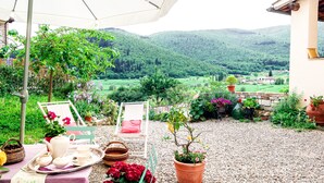En terrasse med et bord dækket til te, omgivet af plantekrukker og en smuk udsigt over en dal.
