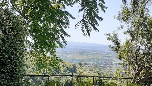 Uma área de estar ao ar livre com cadeiras e mesas verdes, cercada por vegetação exuberante e vista para colinas distantes.