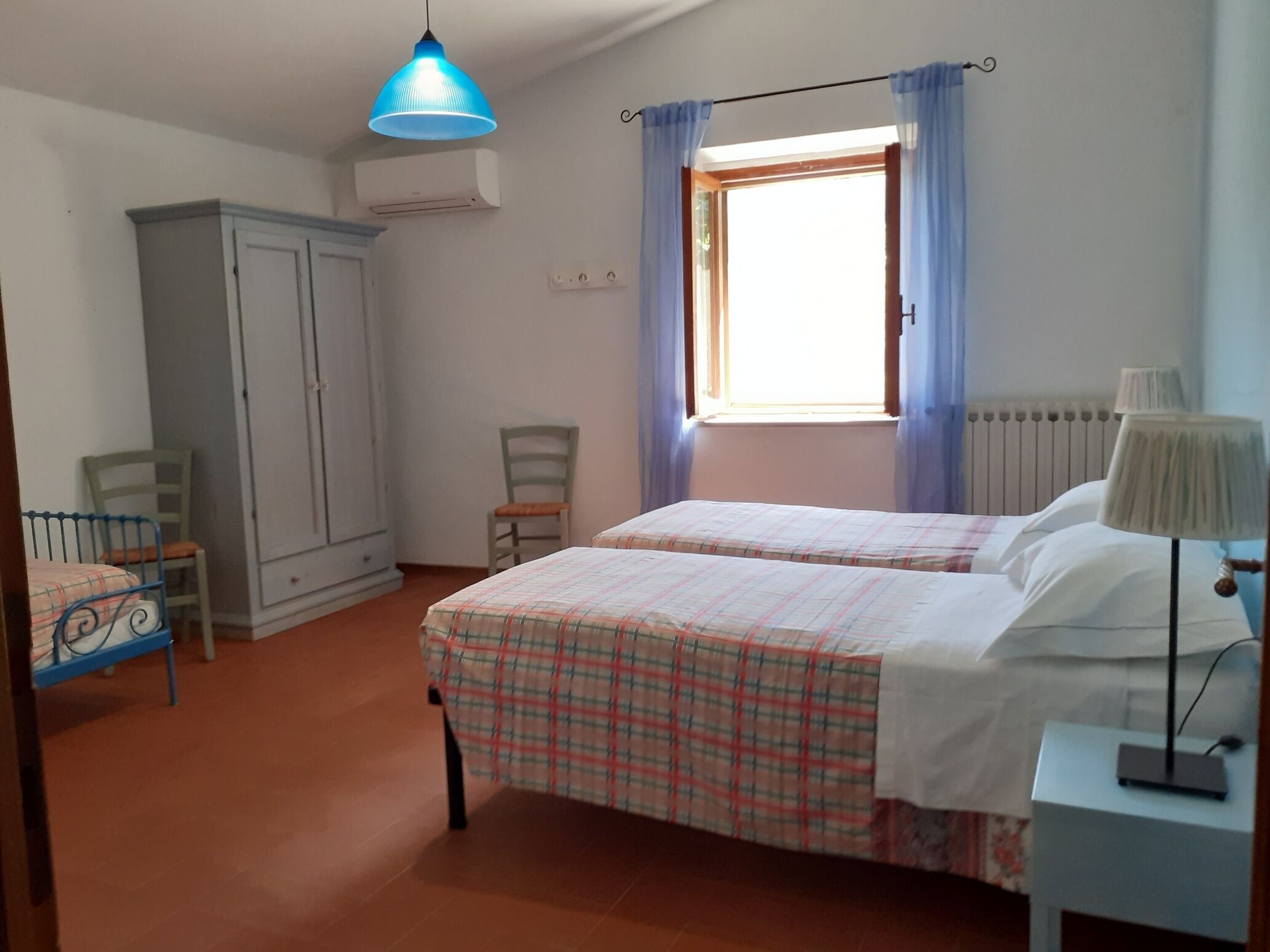 Camera da letto con due letti, un armadio, una sedia, una scrivania con lampada e una finestra con tende.