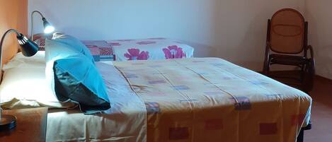 A bedroom with a bed, a desk, a chair, and two wall-mounted paintings.