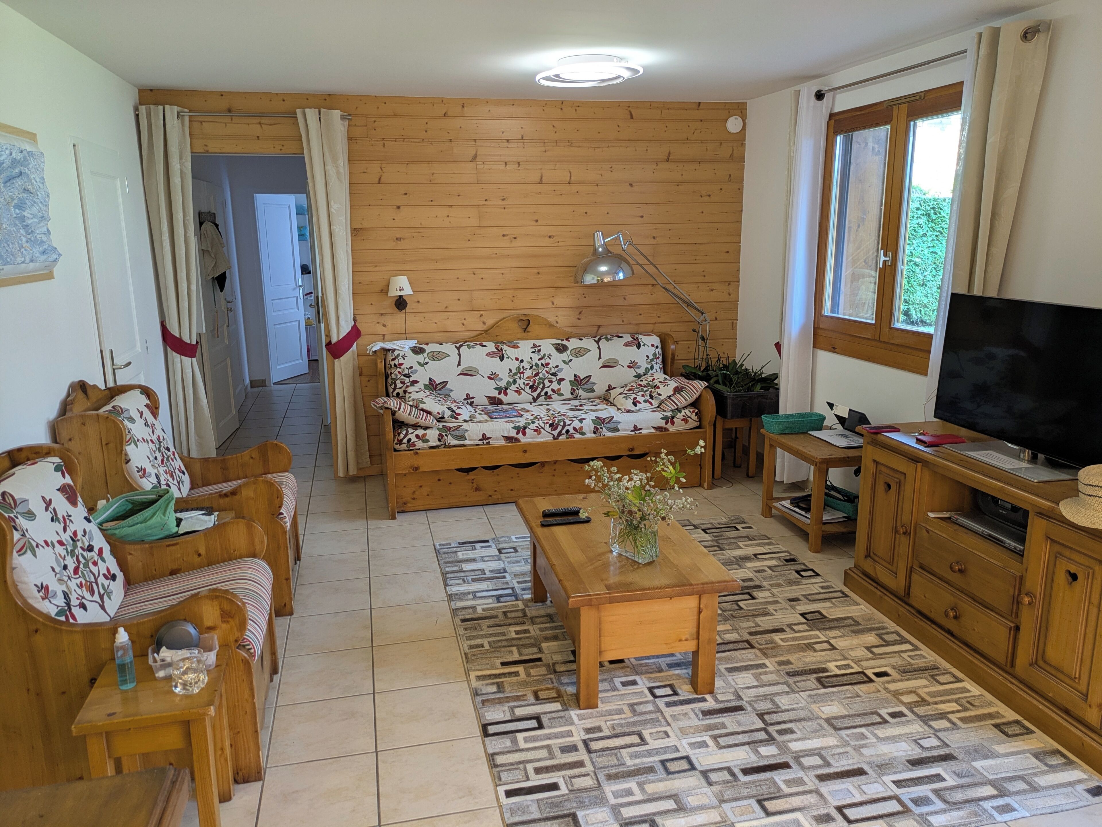 Une pièce aux murs lambrés, comprenant un canapé, des fauteuils, un téléviseur, une lampe et un tapis à motifs.
