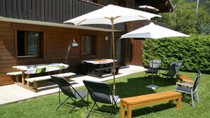 Eine Terrasse im Freien mit einem Holztisch, Bänken und Stühlen, umgeben von einem Holzzaun und Pflanzen.