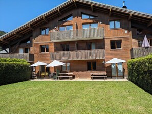 A multi-story wooden chalet with balconies, outdoor seating, and a well-maintained lawn.