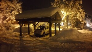 Ein mit Schnee bedecktes Auto steht nachts unter einem Schutzdach.