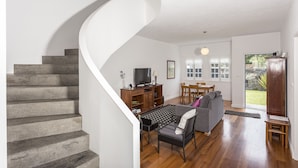 A modern living room with a spiral staircase, a flat-screen TV, a dining area, and a large window with a view of the outdoors. - House of the Camellias, modern constriction - Next to the City Gates (Sete Cidades)