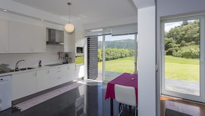A modern kitchen with white cabinets, a stainless steel sink, and a dining area with a table and chairs. - House of the Camellias, modern constriction - Next to the City Gates (Sete Cidades)