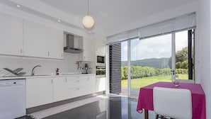 A modern kitchen with white cabinets, a dishwasher, and a dining area with a table covered by a pink tablecloth. - House of the Camellias, modern constriction - Next to the City Gates (Sete Cidades)