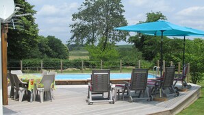 Une terrasse en bois avec des meubles d’extérieur, une piscine et un grand arbre en arrière-plan.
