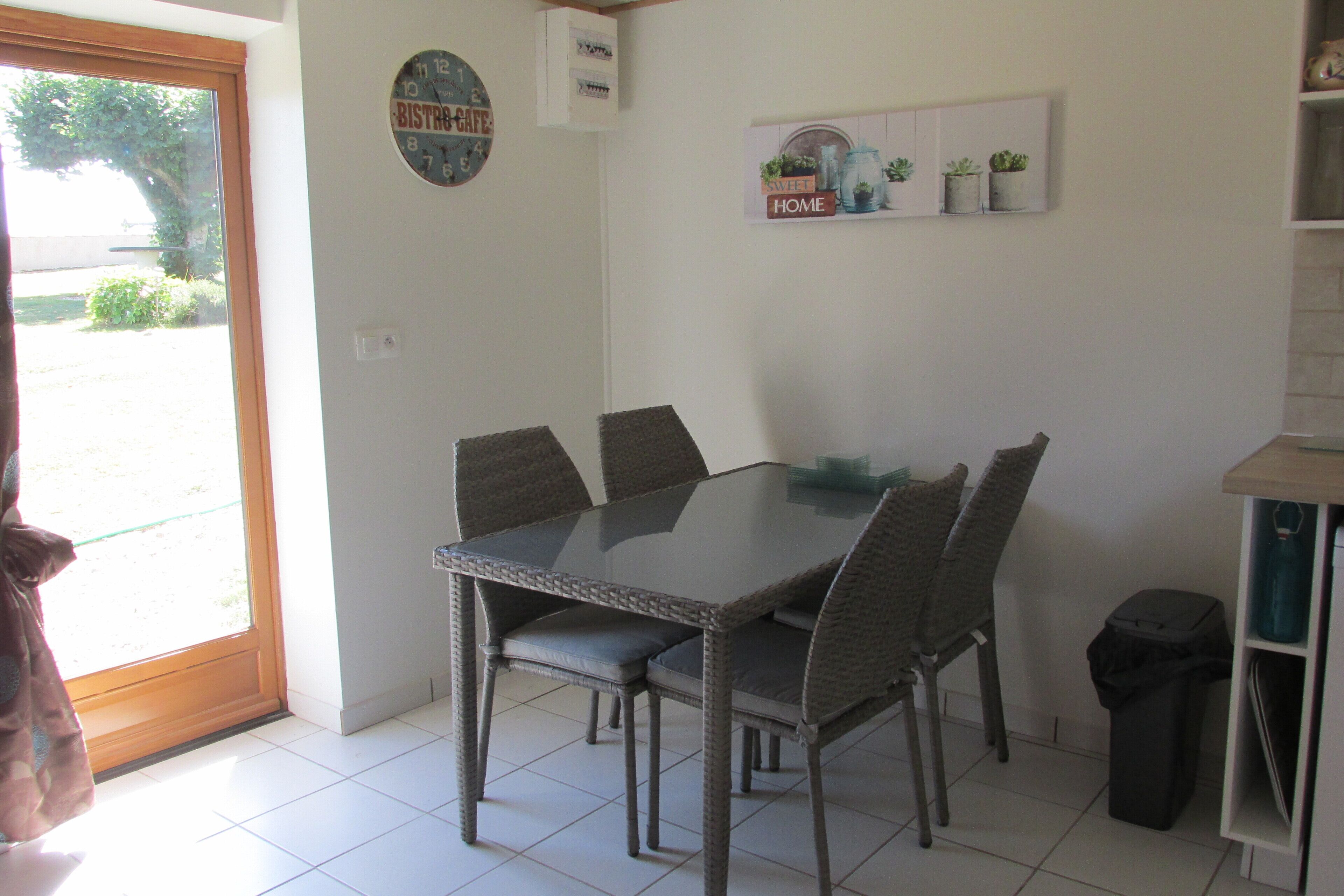 A dining area with a glass-top table and wicker chairs, a trash bin, and a door leading outside.