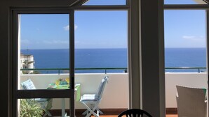 A balcony with a view of the ocean, a table with chairs, and a potted plant.