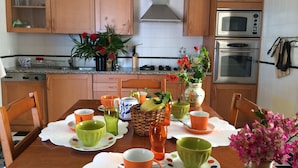 A kitchen with wooden cabinets, a microwave, an oven, and a dining table set with colorful cups and a vase of flowers.