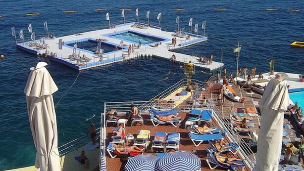 A cruise ship with a pool area and sun loungers on deck.