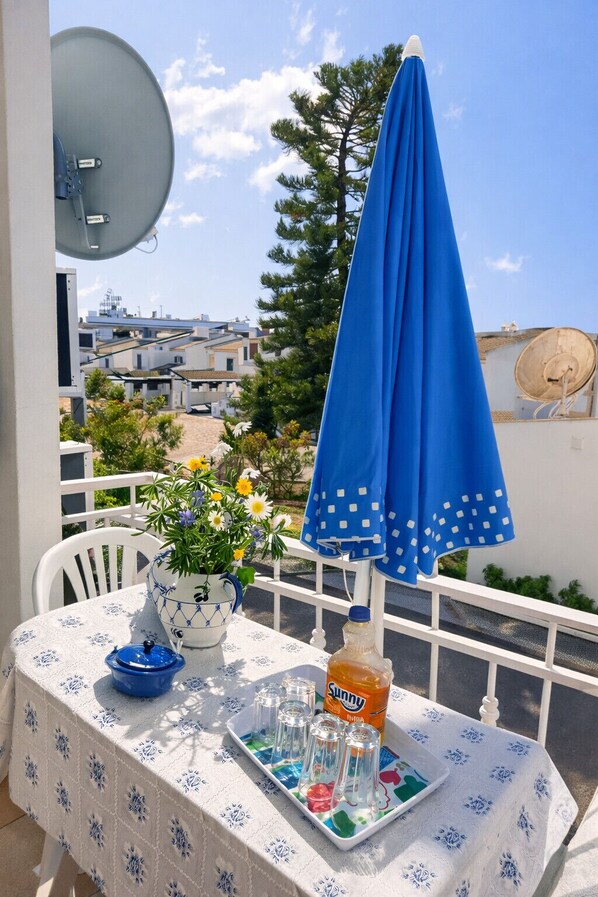 A balcony with a table set for drinks, a blue umbrella, and a satellite dish. - T2 Cond. Privado A/C. piscinas, praia a 500m (Albufeira)