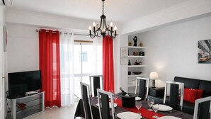 A modern living room with a dining area, a TV, and a chandelier.