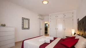 A bedroom with a bed, a wardrobe, a mirror, and an air conditioning unit.