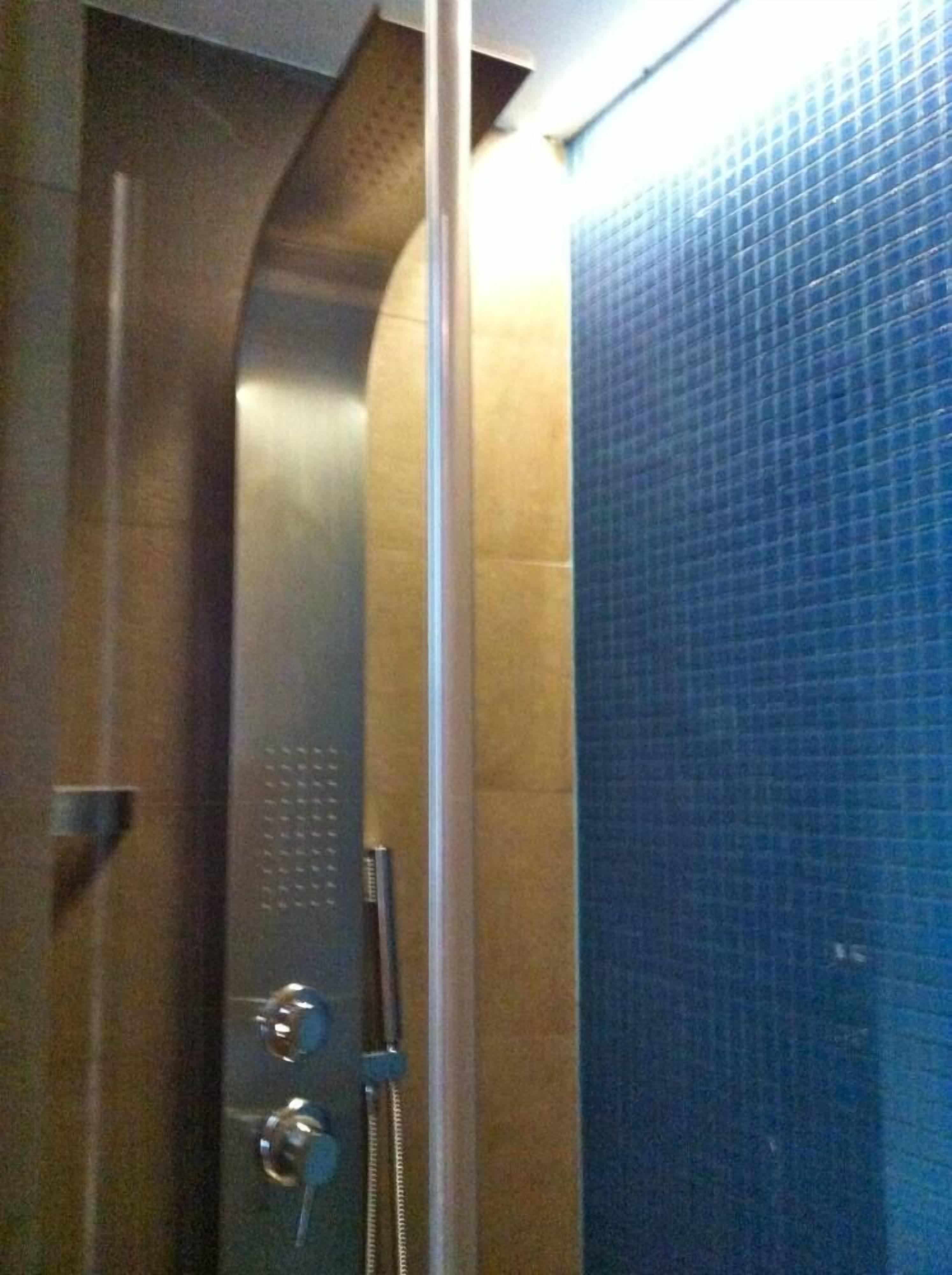 Un espace douche doté d’une porte en verre, d’une poignée en métal et d’un mur recouvert de carreaux bleus.