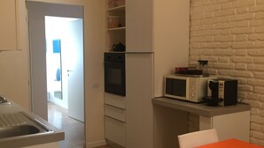 A compact kitchen with a microwave, oven, and white cabinets. A dining table with an orange tablecloth is visible. - Rome: NEW from 3 up to 11 people Central, Modern and bright (Roma)