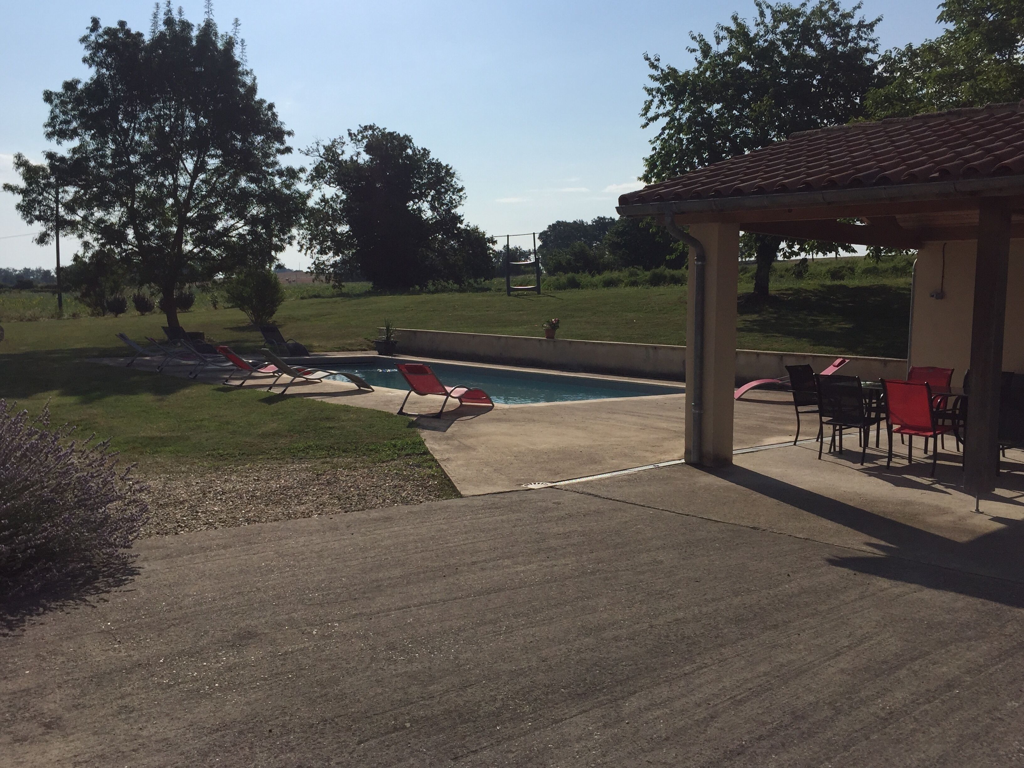 A covered patio area with a pool, outdoor seating, and a view of a grassy field.