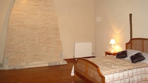 Un dormitorio con techo de madera, una cama con cabecera, una mesita de noche con lámpara y un radiador.