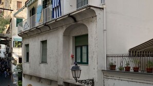 A building with a balcony, a shop on the ground floor, and a mountain in the background.