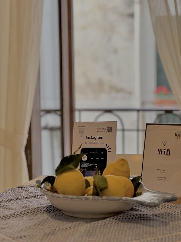 A bowl of lemons on a table with a lace tablecloth, a window with curtains, and two signs, one for Instagram and one for Wifi.