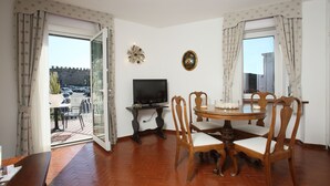 A dining area with a round table, wooden chairs, a television on a stand, and a view of the outside through a glass door.