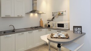 A modern kitchen with white cabinets, a stainless steel range hood, a microwave, and a small bar area with a tray of cups and a picture frame.