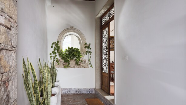 A narrow hallway with a stone wall on one side, a tiled floor, and a wooden door with decorative ironwork.