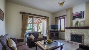 A living room with a sofa, a coffee table with fruit, a TV, and a fireplace. - Villa Astro -  a beach villa with heated pool that sleeps 8 guests  in 4 bedrooms (Paphos)