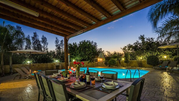 An outdoor dining area with a pool, wooden pergola, and lounge chairs. - Villa Astro -  a beach villa with heated pool that sleeps 8 guests  in 4 bedrooms (Paphos)