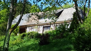 A traditional chalet with a steeply pitched roof, surrounded by lush greenery and trees. - Charming 18th century Normandy House by the river 150 km from Paris (Broglie)