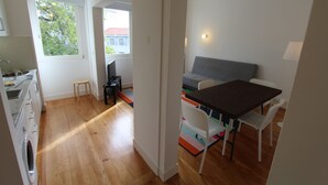 A compact kitchen with a washing machine, a small stool, and a dining area with a table and chairs.