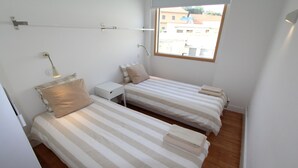 A small, clean room with two beds, a nightstand, and a window.