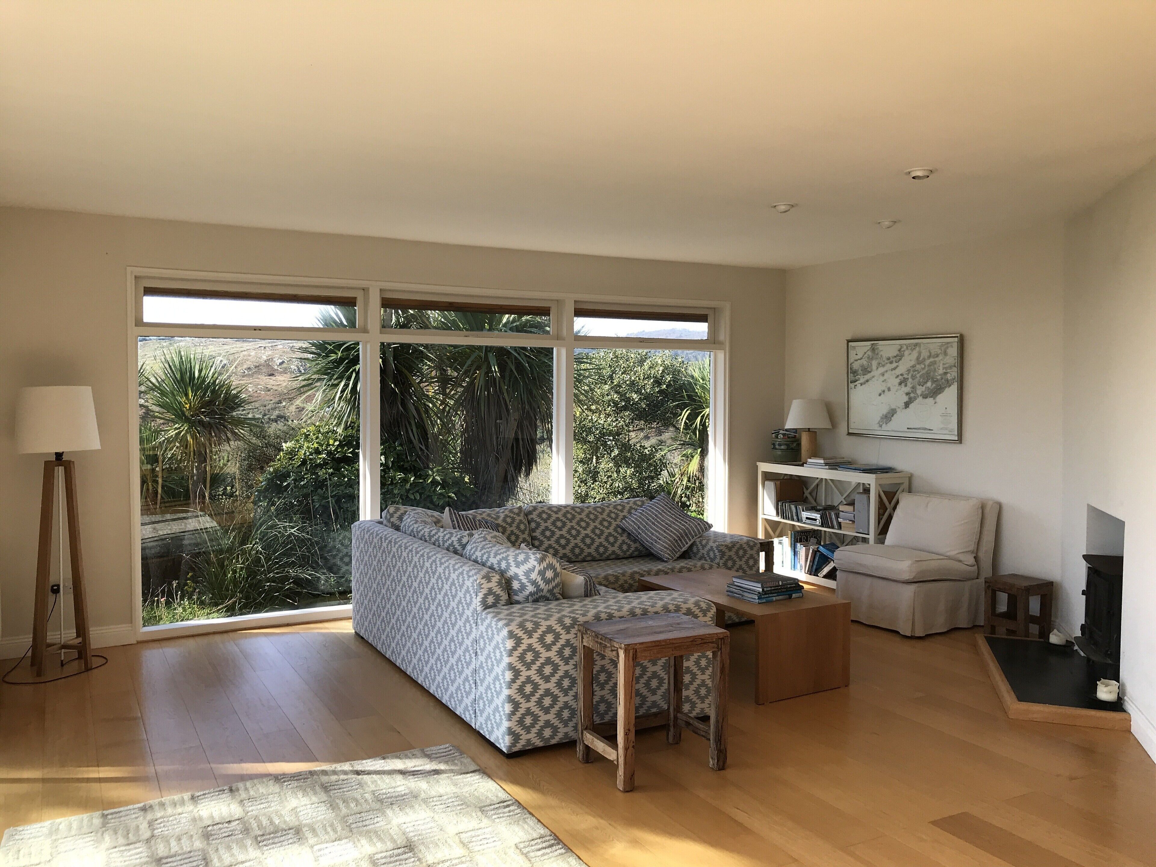 A spacious living room with a large window, a sofa, a coffee table, a lamp, and a bookshelf.